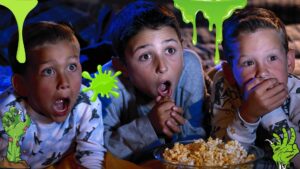 Three young boys watching movie and eating popcorn