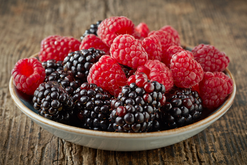 A bowl of raspberries and blackberries, on a wooden table