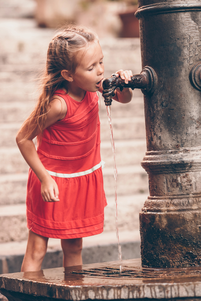 Little girl drinking water from a cistern